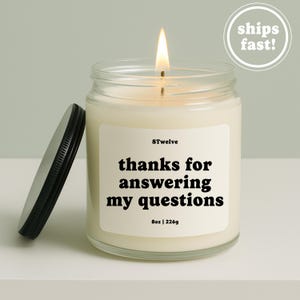 May include: A clear glass candle jar with a lit wick and a black metal lid resting beside it. The white label features the text 8Twelve, thanks for answering my questions, and 8oz | 226g in bold black lettering against a cream background.