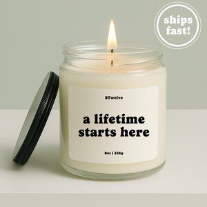 May include: A clear glass candle jar with a lit wick and a black metal lid placed to the side. The white label features the text 8Twelve, a lifetime starts here, and 8oz | 226g. The wax is off-white and the flame is bright yellow and orange.