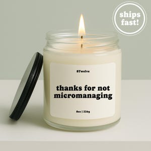 Pode incluir: Uma vela num frasco de vidro transparente com um pavio aceso e uma tampa de metal preta ao lado. O rótulo branco apresenta o texto 8Twelve, thanks for not micromanaging, e 8oz | 226g em preto. A cera da vela é de cor branco-sujo.
