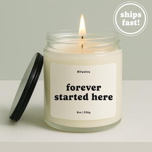 May include: A clear glass candle jar with a lit wick and a black metal lid resting beside it. The white label features the text 8Twelve, forever started here, and 8oz | 226g. The wax is off-white, and the flame is bright yellow and orange.