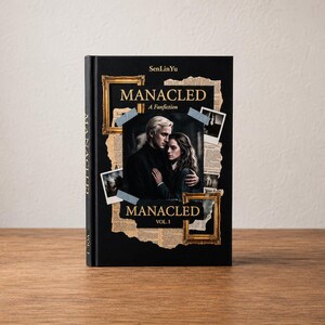 Op de afbeelding: Een zwart gebonden boek getiteld Manacled door SenLinYu, Vol. 1. De kaft bevat een centrale foto van een man en vrouw die elkaar omhelzen, omringd door collage-elementen zoals krantenknipsels, gouden fotolijsten en kleine foto's.