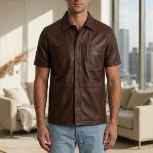 Puede incluir: Una camisa de manga corta de color marrón oscuro hecha de un material liso con cuello clásico, cierre frontal de botones y dos bolsillos en el pecho. La camisa se combina con pantalones vaqueros azul claro para un look sencillo y limpio.