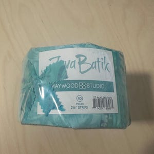 May include: A roll of turquoise Java Batik fabric strips by Maywood Studio, wrapped in clear plastic. The label indicates 40 pieces of 2 1/2 inch strips, model number ST-MASJAB-TUQ, with a barcode and the brand name clearly printed on the front.