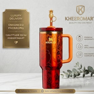 Puede incluir: Un vaso Stanley rojo con estampado floral, tapa dorada y un adorno en forma de piña. El vaso incluye un asa lateral, el logotipo de Stanley y texto que incluye KHEEROMART, PREMIUM WARRANTY, 100% SPILL-PROOF LID y ERGONOMIC COMFORT GRIP.