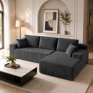 May include: A dark gray corduroy sectional sofa featuring a chaise lounge, three large back cushions, and two smaller square throw pillows. The fabric has a distinct vertical ribbed texture throughout the entire surface of the furniture piece.