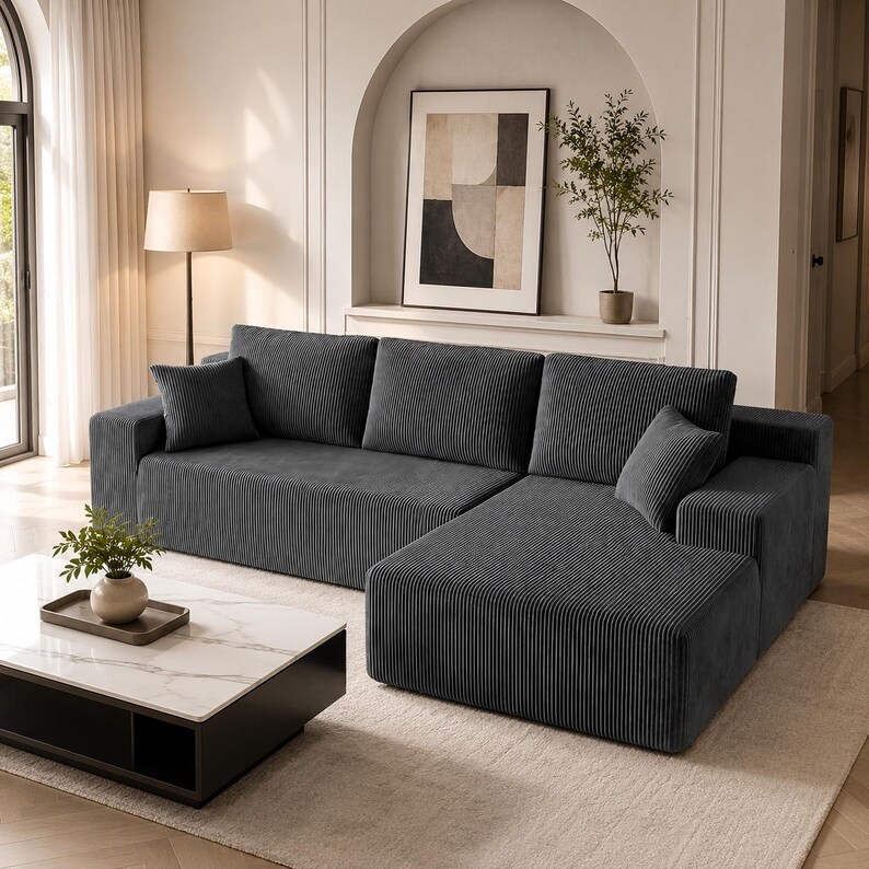 May include: A dark gray corduroy sectional sofa featuring a chaise lounge, three large back cushions, and two smaller square throw pillows. The fabric has a distinct vertical ribbed texture throughout the entire surface of the furniture piece.