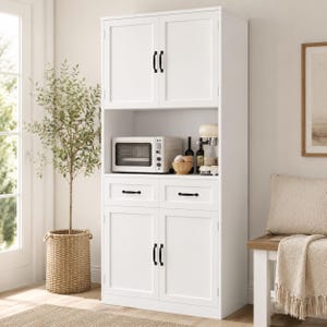 May include: A tall white kitchen pantry cabinet featuring two upper doors, two central drawers, and two lower doors, all equipped with black metal handles. The open middle shelf houses a microwave, a small wooden bowl, and a coffee machine.