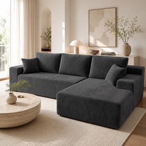 May include: A dark gray sectional sofa upholstered in a textured corduroy fabric. The sofa features a chaise lounge section on the right side, three large back cushions, and two matching square throw pillows positioned on the ends.