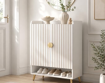 May include: A white shoe cabinet featuring vertical slats with gold accents, two doors with a circular gold handle, and an open bottom shelf. The cabinet stands on four tapered gold legs and contains several pairs of neutral-colored sneakers.