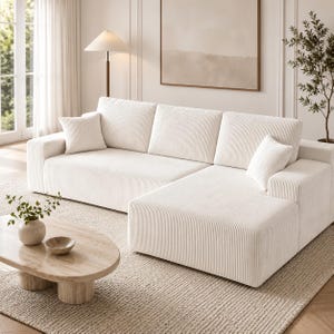 May include: A cream-colored sectional sofa with a corduroy texture, featuring a chaise lounge section, three back cushions, and two square throw pillows. The sofa has a low-profile design with wide armrests and a clean, structured silhouette.