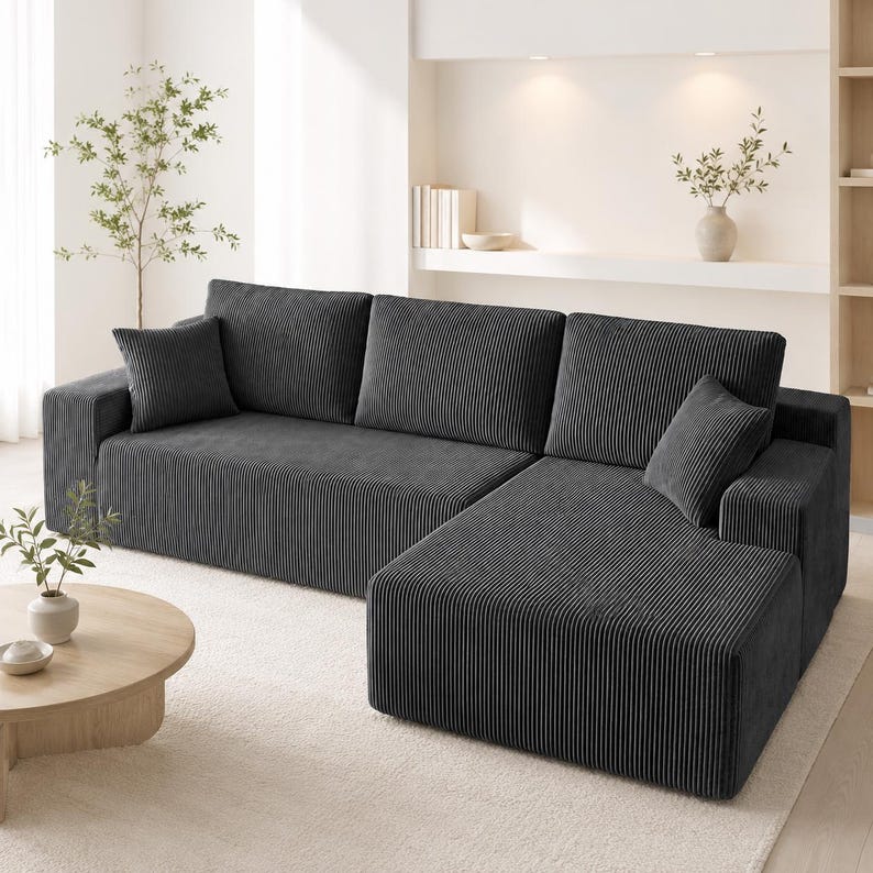 May include: A dark gray sectional sofa upholstered in a textured corduroy fabric. The sofa features a chaise lounge on the right side, three large back cushions, and two square throw pillows, all covered in the same ribbed material.