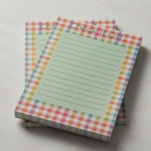 May include: A rectangular notepad with a light green center featuring horizontal lines and the text Check It Off printed at the top. The border consists of a colorful multi-colored gingham plaid pattern in shades of pink, yellow, blue, and orange.