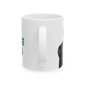 Puede incluir: Una taza de cer&aacute;mica blanca con un asa vertical en el lado derecho. El lateral de la taza muestra el texto en verde "I NOTICE YOU" en letras may&uacute;sculas. A la derecha del asa, se observa una vista parcial de una ilustraci&oacute;n gr&aacute;fica oscura.
