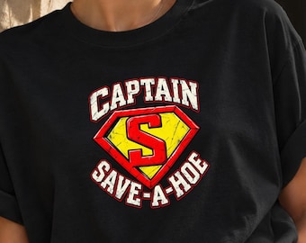 Könnte beinhalten: Ein schwarzes T-Shirt mit kurzen Ärmeln und einem Grafikdruck eines gelb-roten rautenförmigen Emblems mit einem großen roten Buchstaben S in der Mitte. Der Text CAPTAIN SAVE-A-HOE ist in weißen Blockbuchstaben darum gedruckt.