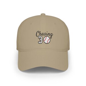 May include: A khaki baseball cap featuring an embroidered design on the front. The embroidery includes the black text "Chasing" above the number "30" in white with black outlines, and a white baseball with red stitching next to the number.