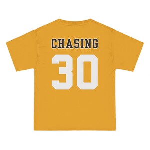 May include: A mustard yellow short-sleeve t-shirt featuring the word CHASING in black block letters above the large white number 30. The design is centered on the back of the garment, which has a crew neckline and a standard straight hem.