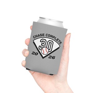 May include: A grey foam can cooler featuring a black and white graphic of a baseball home plate with the number 30, a baseball illustration, and the text CHASE COMPLETE 20 26 printed in black lettering across the front surface of the sleeve.