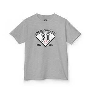May include: A heather gray short-sleeve t-shirt featuring a graphic of a baseball home plate with the number 30, a baseball, and the text CHASE COMPLETE 20 26 printed in black and white on the center of the chest area of the garment.