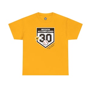 May include: A mustard yellow short-sleeve t-shirt featuring a graphic of a home plate with the text MISSION ACCOMPLISHED, the number 30, a baseball, a yellow star with a checkmark, and the text MAJOR LEAGUE BALLPARKS in black and white.