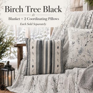 Könnte beinhalten: Eine Birch Tree Black Decke und zwei passende Kissen. Ein Kissen hat ein vertikales Streifenmuster mit Blattakzenten, während das andere und die Decke einen Druck mit grauen und weißen Birkenzweigen zeigen. Text lautet Birch Tree Black.