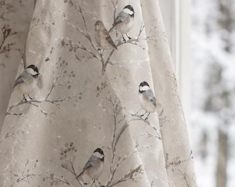 May include: A beige kitchen towel featuring a repeating pattern of small birds perched on thin, bare branches. The fabric has a soft, neutral tone with detailed illustrations of birds in shades of black, white, and gray, hanging from a black hook.