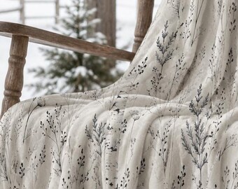 May include: A cream-colored throw blanket featuring a dark gray botanical print of wildflowers and grasses draped over a wooden rocking chair. The fabric displays a repeating pattern of delicate stems, leaves, and seed heads across the surface.