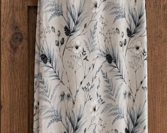 May include: A rectangular kitchen towel featuring a repeating pattern of blue and grey botanical illustrations, including pine needles, small berries, and delicate flowers, hanging from a bronze-colored metal handle on a wooden cabinet.
