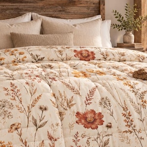 May include: A cream-colored comforter featuring a botanical print of wildflowers in shades of rust, orange, and brown. The bedding is draped over a bed with a wooden headboard, accompanied by beige pillows and a textured brown knit throw blanket.