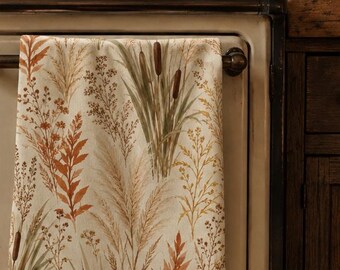 May include: A rectangular kitchen towel featuring a botanical print of dried grasses, cattails, and autumn-colored leaves in shades of rust, gold, and sage green on a cream background, hanging from the handle of a vintage-style cream-colored stove.