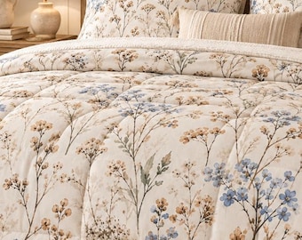 May include: A bedding set featuring a cream-colored comforter and matching pillow shams decorated with a botanical print of small blue and tan wildflowers. The set includes a solid tan rectangular accent pillow and plain cream pillows.