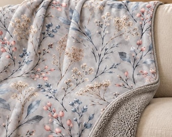 May include: A fleece sherpa blanket with a gray backing option, featuring a light gray surface printed with a botanical pattern of blue leaves, pink berries, and white wildflowers. The text Fleece Sherpa Blanket Gray Backing Option is visible.