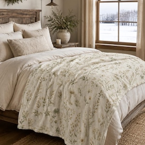 Bedroom:
Field sage and cream wildflower blanket draped across a rustic farmhouse bed with neutral bedding and natural wood furniture.
