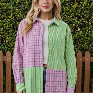 May include: A long-sleeve button-down shirt featuring a color-blocked design with alternating panels of pink and blue plaid and green and white vertical stripes. The shirt includes a collar, a front button placket, and a chest pocket.