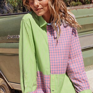 May include: A long-sleeve button-down shirt featuring a color-blocked design. One side displays vertical lime green and white stripes, while the other side and cuffs feature a pink and blue plaid pattern. The shirt has a classic collar.