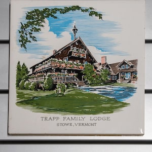 Könnte beinhalten: Eine quadratische Keramikfliese mit einer detaillierten Illustration der Trapp Family Lodge in Stowe, Vermont. Das Bild zeigt ein mehrstöckiges Holzgebäude mit Balkonen, Blumenkästen, grünen Rasenflächen und blauem Himmel. Der Text lautet Trapp Family Lodge Stowe, Vermont.