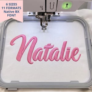 May include: An embroidery machine hoop holding white fabric with the name Natalie stitched in pink cursive thread. A pink banner in the top left corner displays the text 6 SIZES 11 FORMATS NATIVE BX FONT. The machine needle is visible.