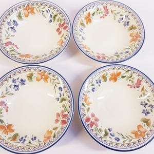 Puede incluir: Cuatro cuencos de cerámica blanquecina con un diseño floral. Los cuencos tienen un borde azul con un patrón geométrico y están decorados con flores naranjas, rosas y azules y hojas verdes. Los cuencos están dispuestos en un cuadrado.