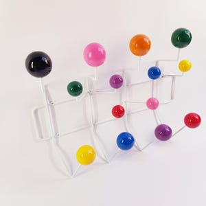 May include: A wall-mounted coat rack featuring a white metal wire frame with multiple protruding arms. Each arm is tipped with a smooth, glossy sphere in various colors including black, pink, green, yellow, orange, purple, blue, and red.