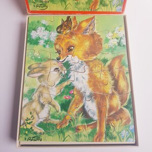 May include: A vintage jigsaw puzzle featuring a fox and a rabbit. The fox is brown and white with a bushy tail. The rabbit is brown and white with long ears. The puzzle pieces are arranged in a woodland setting with green trees and flowers.