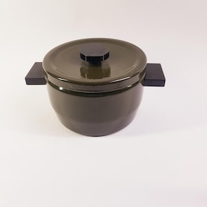 May include: A dark olive green ceramic cooking pot with a matching lid and a black knob. The pot has two rectangular black handles on either side. The pot is designed for cooking and serving.