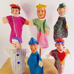 May include: A collection of six hand puppets featuring diverse characters with painted plastic heads and fabric clothing. The figures include a person in a red hat, a crowned queen, a person in a green hat, a person in a striped shirt, a person in a blue cap, and a person in a red cap.