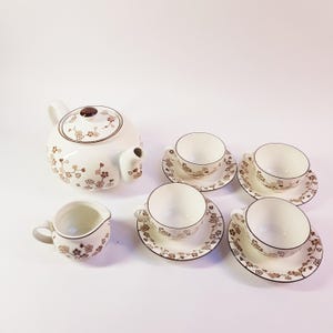 May include: A vintage tea set featuring a white teapot, creamer, and four teacups with saucers. The set has a brown floral pattern and brown trim. The teapot has a brown lid and spout. The teacups are small.