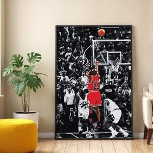 Pode incluir: Uma impressão de arte de parede vertical emoldurada com uma fotografia a preto e branco de um jogo de basquetebol com uma multidão ao fundo. Um jogador com uma camisola vermelha com o número 23 salta para lançar a bola ao cesto.
