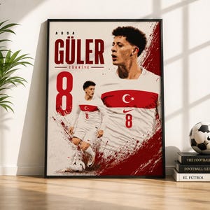 May include: A framed poster featuring a graphic illustration of soccer player Arda Güler in a white and red Turkey national team kit. The design includes the text ARDA GÜLER, TÜRKİYE, and the number 8, set against a white background with red paint splatter accents.