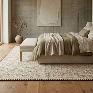 Pode incluir: Um quarto com uma cama estofada em bege com roupa de cama em verde-oliva e creme, um banco a condizer ao fundo da cama, uma mesa de cabeceira de madeira com candeeiro e um grande tapete retangular creme com uma borda castanha escura.