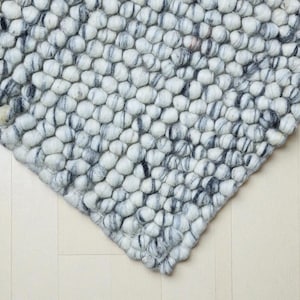 May include: A rug constructed from numerous small, spherical felted wool balls. The balls are arranged in a dense, uniform pattern and feature a color palette of solid white, light gray, and dark charcoal gray, creating a mottled appearance.