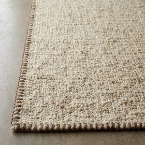 Close-up of a handmade handwoven wool rug featuring a soft textured weave in ivory and beige tones with a modern minimalist design for living room and bedroom decor."