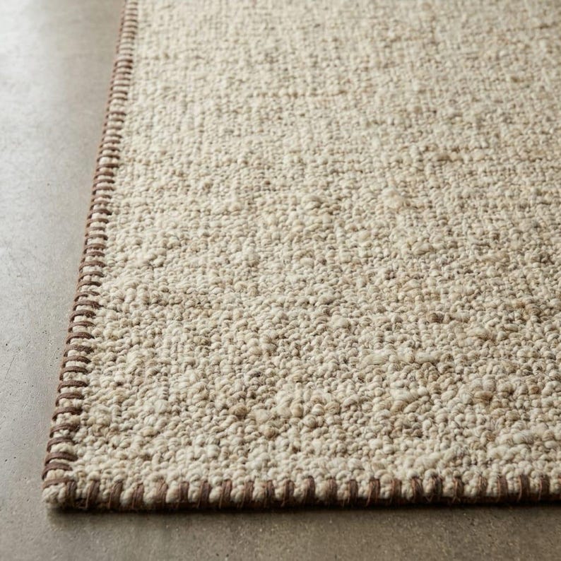 Close-up of a handmade handwoven wool rug featuring a soft textured weave in ivory and beige tones with a modern minimalist design for living room and bedroom decor."