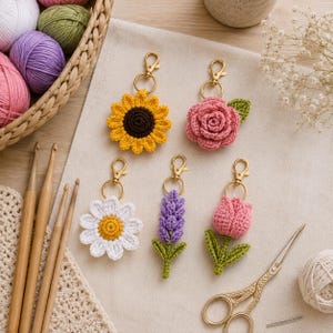 May include: Five crochet flower keychains featuring a yellow sunflower with a brown center, a pink rose with a green leaf, a white daisy with a yellow center, a purple lavender sprig with green leaves, and a pink tulip with green leaves.