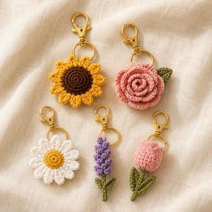 May include: Five crochet flower keychains with gold-tone lobster clasps. The set includes a yellow sunflower with a brown center, a pink rose with a green leaf, a white daisy with a yellow center, a purple lavender sprig, and a pink tulip with green leaves.